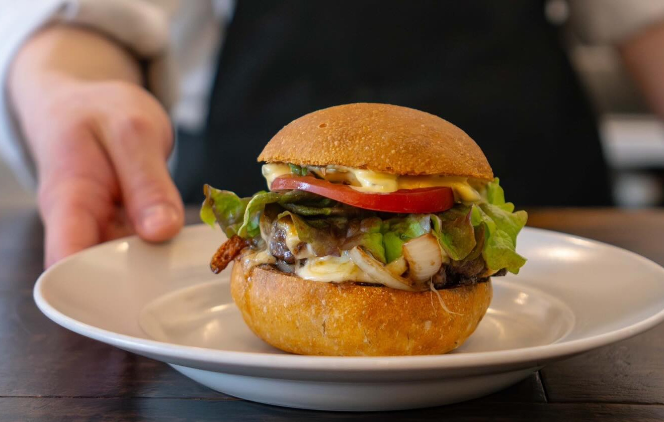 皿に盛られたハンバーガーに手を添える店のスタッフ